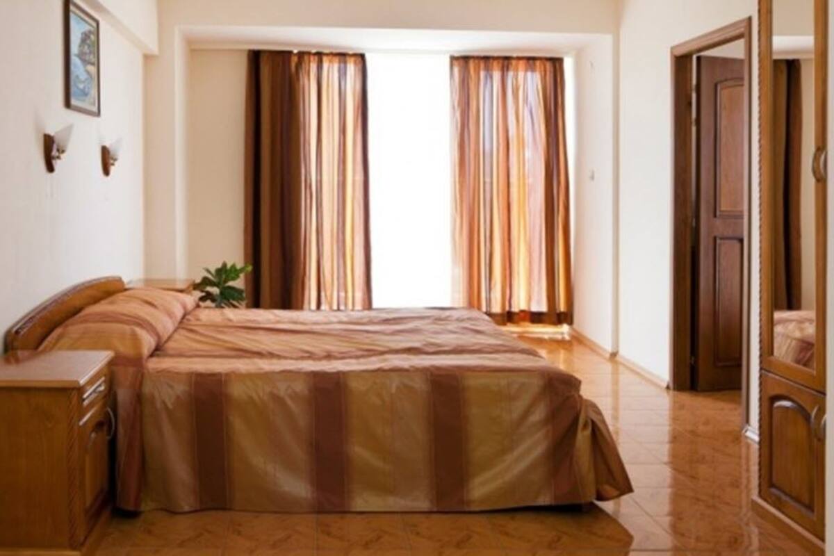 A bedroom with a bed, a nightstand, a wooden cabinet, and a window with curtains.