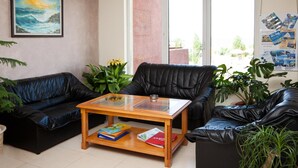 A living room with two black leather sofas, a wooden coffee table with books, and a painting on the wall. - Hotel Sunny (Sozopol)