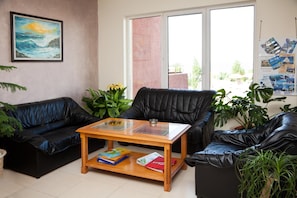 A living room with two black leather sofas, a wooden coffee table with books, and a painting on the wall. - Hotel Sunny (Sozopol)