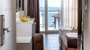 A modern hotel room with a balcony, a desk with a chair, and a bed with a brown headboard. - Hotel Sunny (Sozopol)