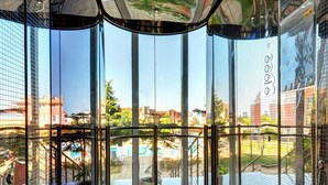A modern atrium with large glass windows, a pool, and a view of surrounding buildings. - Hotel Sunny (Sozopol)