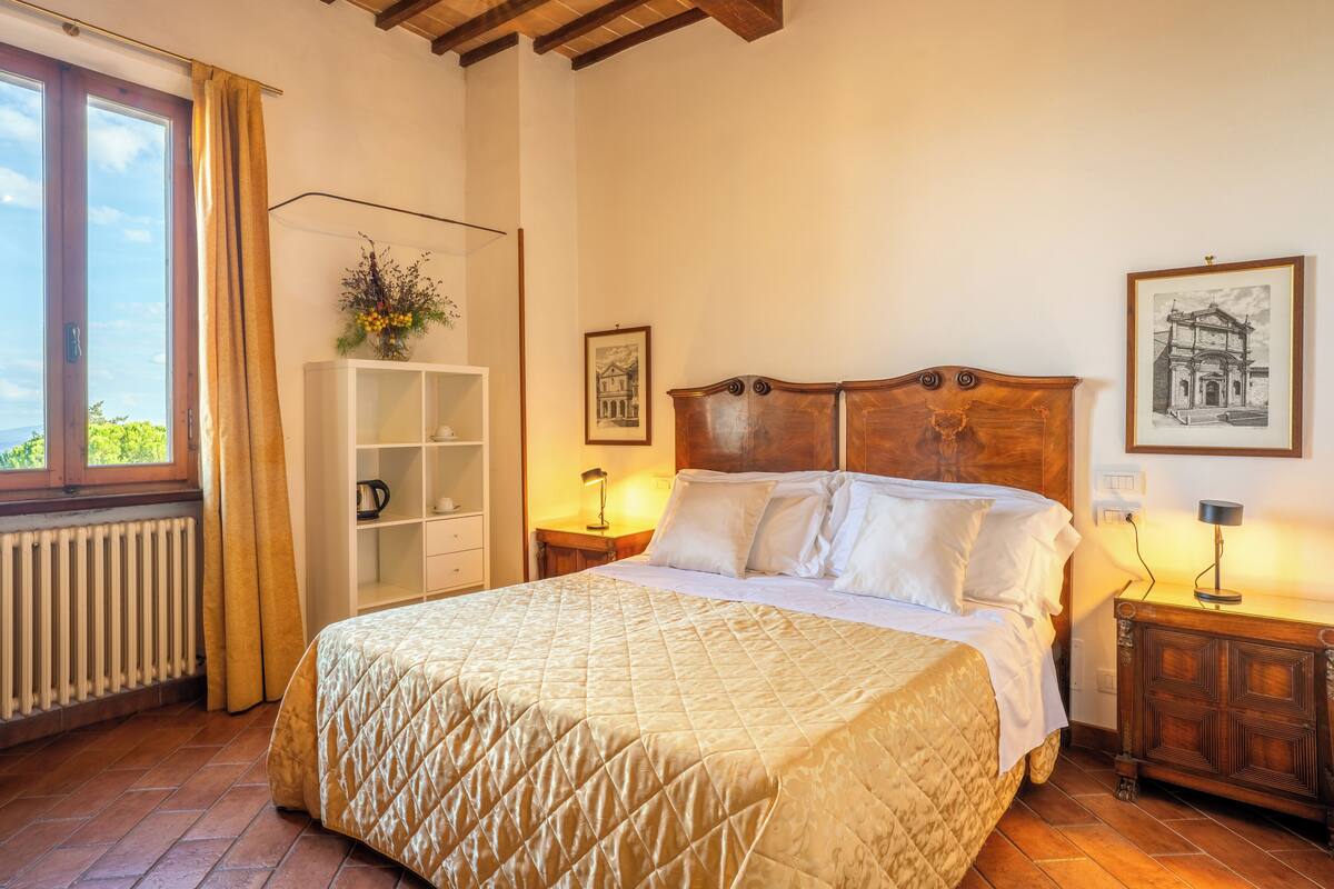 Een slaapkamer met een groot bed, een houten hoofdbord, een witte garderobe, een nachtkastje met een lamp en een raam met gordijnen.