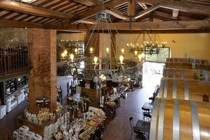 A spacious interior with exposed wooden beams, a large chandelier, and various tables and chairs.