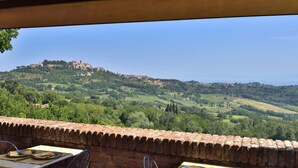 An outdoor dining area with tables and chairs, overlooking a lush green landscape and a hill with buildings. - La Corte Medicea (Montepulciano)