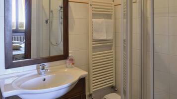 Un baño con lavamanos, espejo, ducha y toallero.