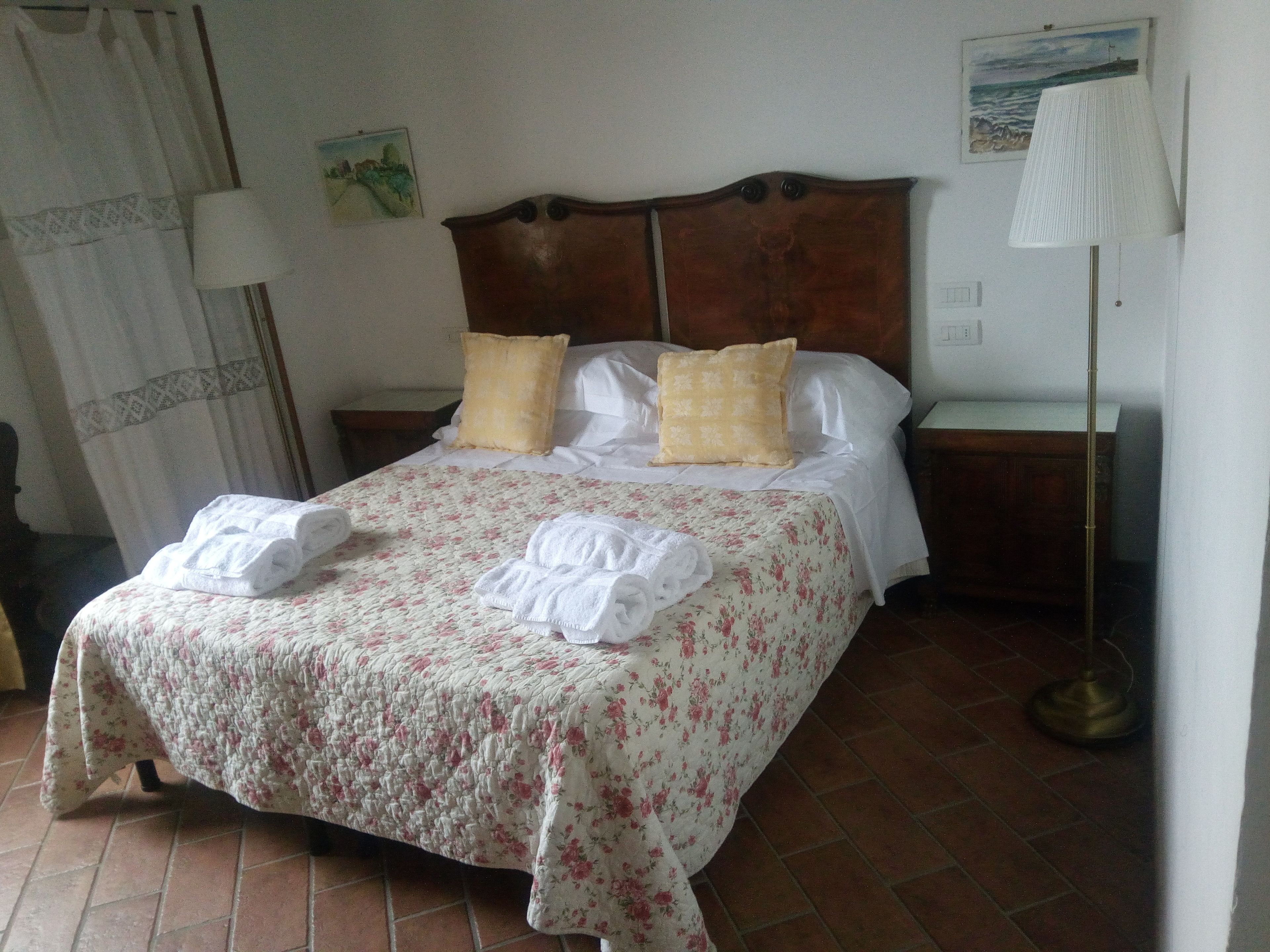 A neatly made bed with floral bedding, two pillows, and two folded towels.