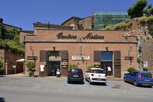 A brick building with the sign "Cantina Medice" and "Ristorante La Corcetta" on the facade. There are two cars parked in front, and a blue car is parked on the right side.