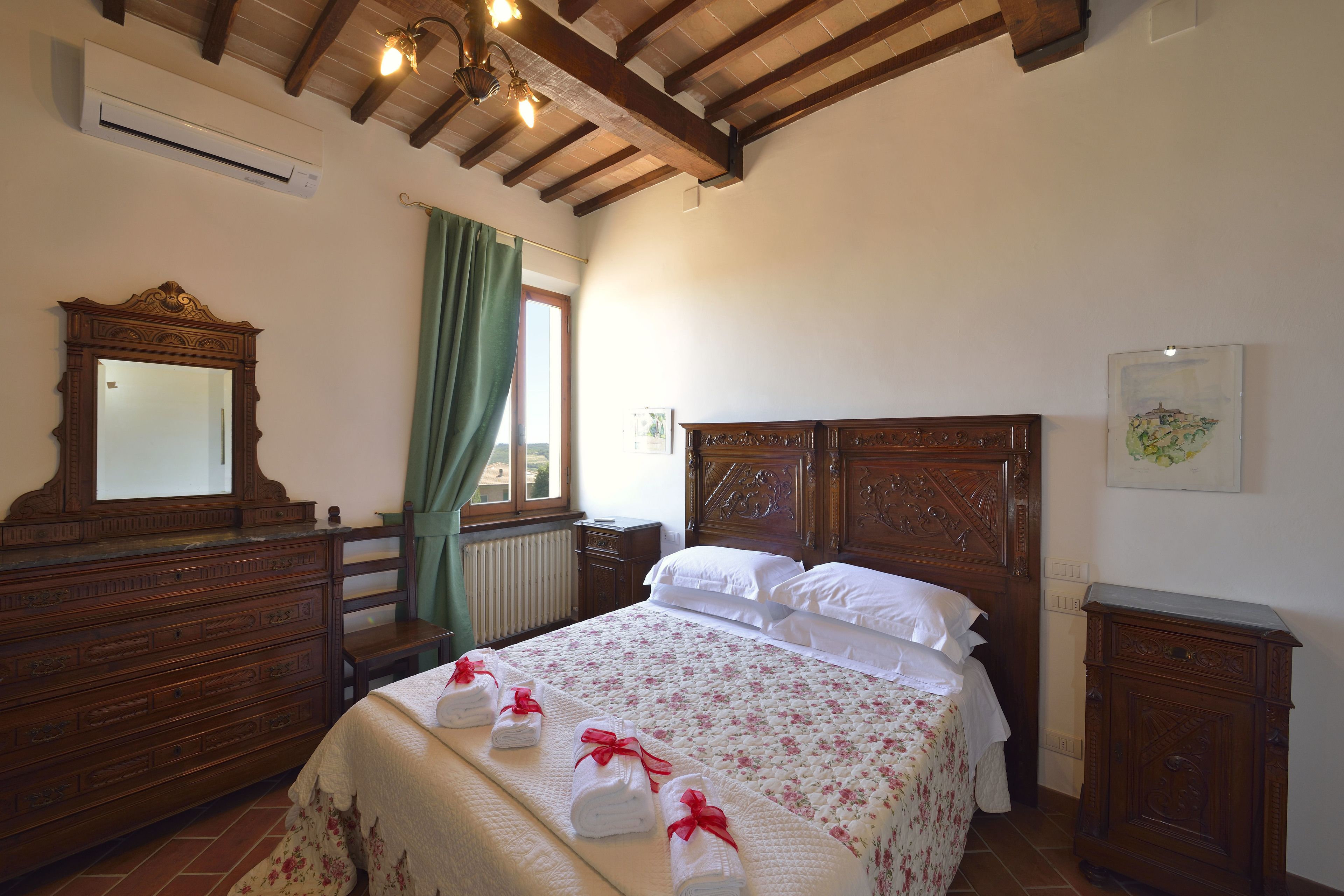 Un dormitorio con cama de madera, cómoda, espejo y ventana con cortinas.