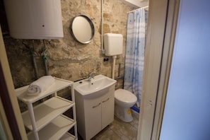 A bathroom with a stone wall, a white sink, a toilet, and a shower curtain. - Hostel Omiš (Omis)