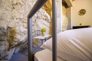 A bunk bed in a room with a stone wall, a small table with a plant, and a mirror on the wall. - Hostel Omiš (Omis)