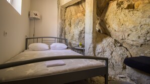 A bed in a room with a stone wall, a bedside table with a lamp, and a small plant.