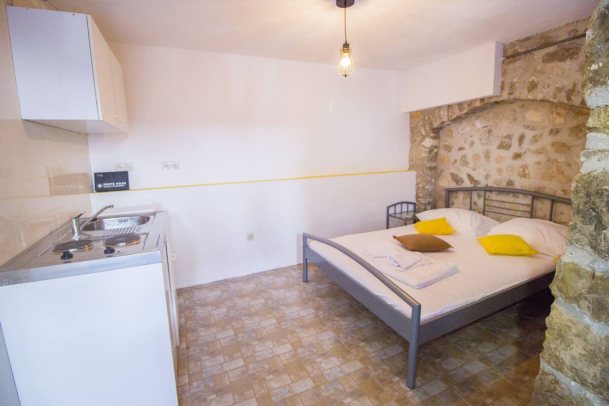 Una habitación compacta con cama, una pequeña kitchenette y una pared de piedra.