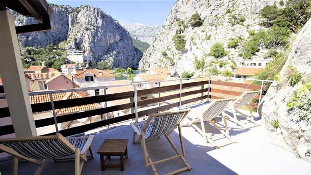A terrace with hammocks and a table, overlooking a mountainous landscape with buildings.