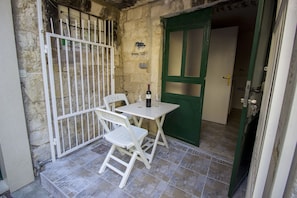 A small outdoor seating area with a table and chairs, a bottle of wine, and a green door. - Hostel Omiš (Omis)
