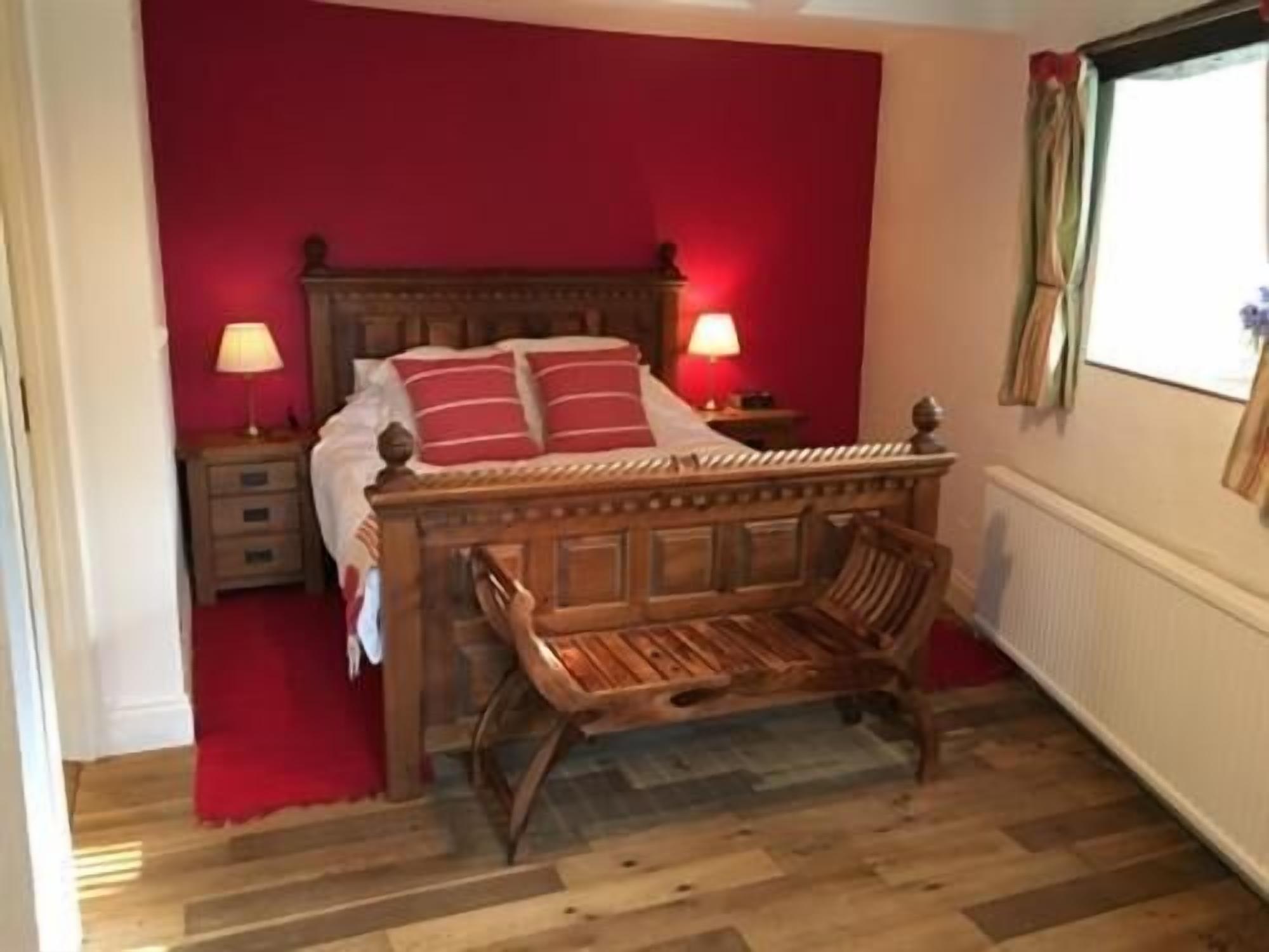 Une chambre à coucher avec un lit en bois, des murs rouges, deux lampes de chevet et une fenêtre avec des rideaux.