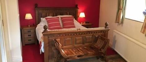 Un dormitorio con cama de madera, paredes rojas, dos lámparas de noche y una ventana con cortinas.