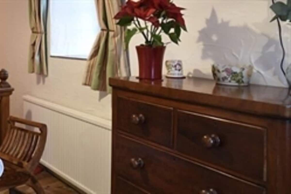 A wooden bed with a headboard, two bedside lamps, a wooden chair, a wooden dresser, and a potted plant.