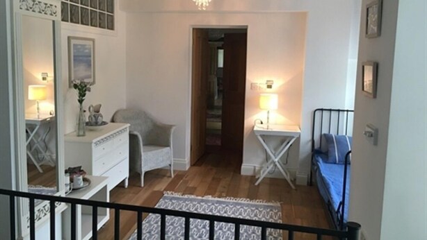 A room with a wooden floor, a white dresser, a chair, a small table with a lamp, and a blue sofa. - Stoneleigh Barn B&B (Sherborne)