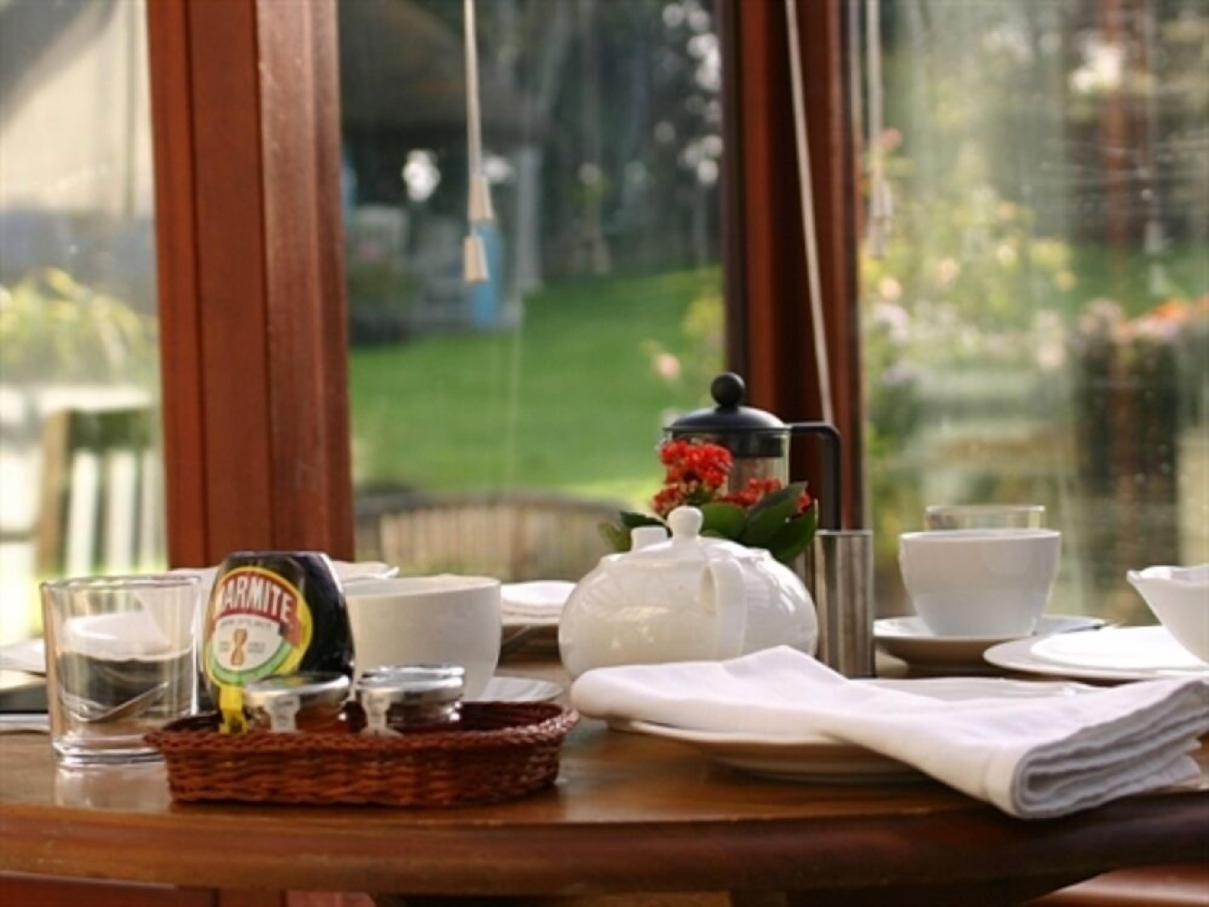 A table set with a coffee pot, teapot, cups, and a jar of Marmite.
