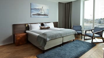 A modern hotel room with a large bed, a view of the city through the window, and a painting of a ship on the wall.