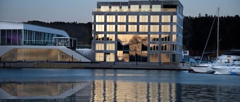 Un bâtiment moderne doté d’une façade en verre, d’un toit plat et dont l’image se reflète dans l’eau.