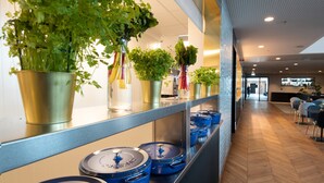 A modern kitchen with stainless steel countertops, blue pots, and potted herbs on shelves.