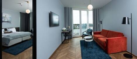 A modern hotel room with a bed, a red sofa, a small table, and a TV.