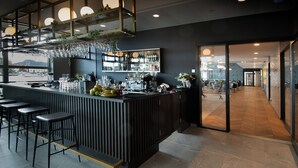 A modern bar area with a dark counter, bar stools, and a variety of bottles and glasses. - Mandal Hotel (Lindesnes)