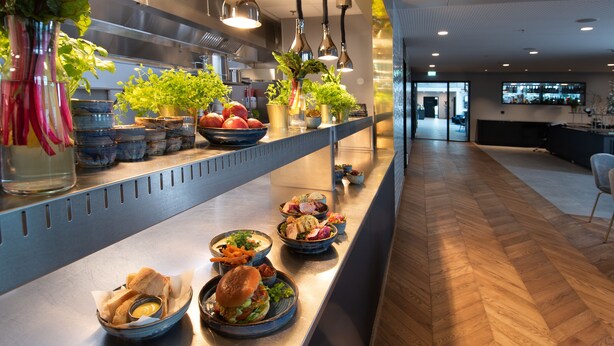 A modern kitchen with a long counter displaying various food items and plants. - Mandal Hotel (Lindesnes)