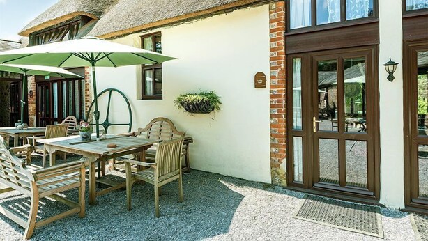 Een terras met houten tafels en stoelen, een groene parasol en een hangplanter.