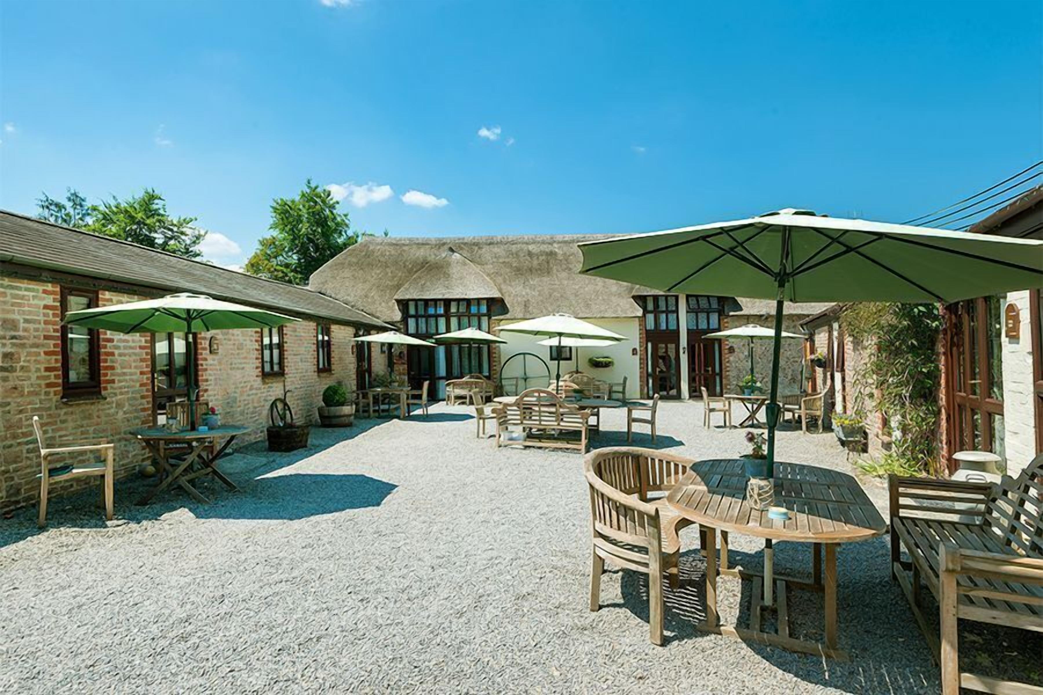 An outdoor patio area with tables and chairs, surrounded by brick buildings and thatched-roof structures.