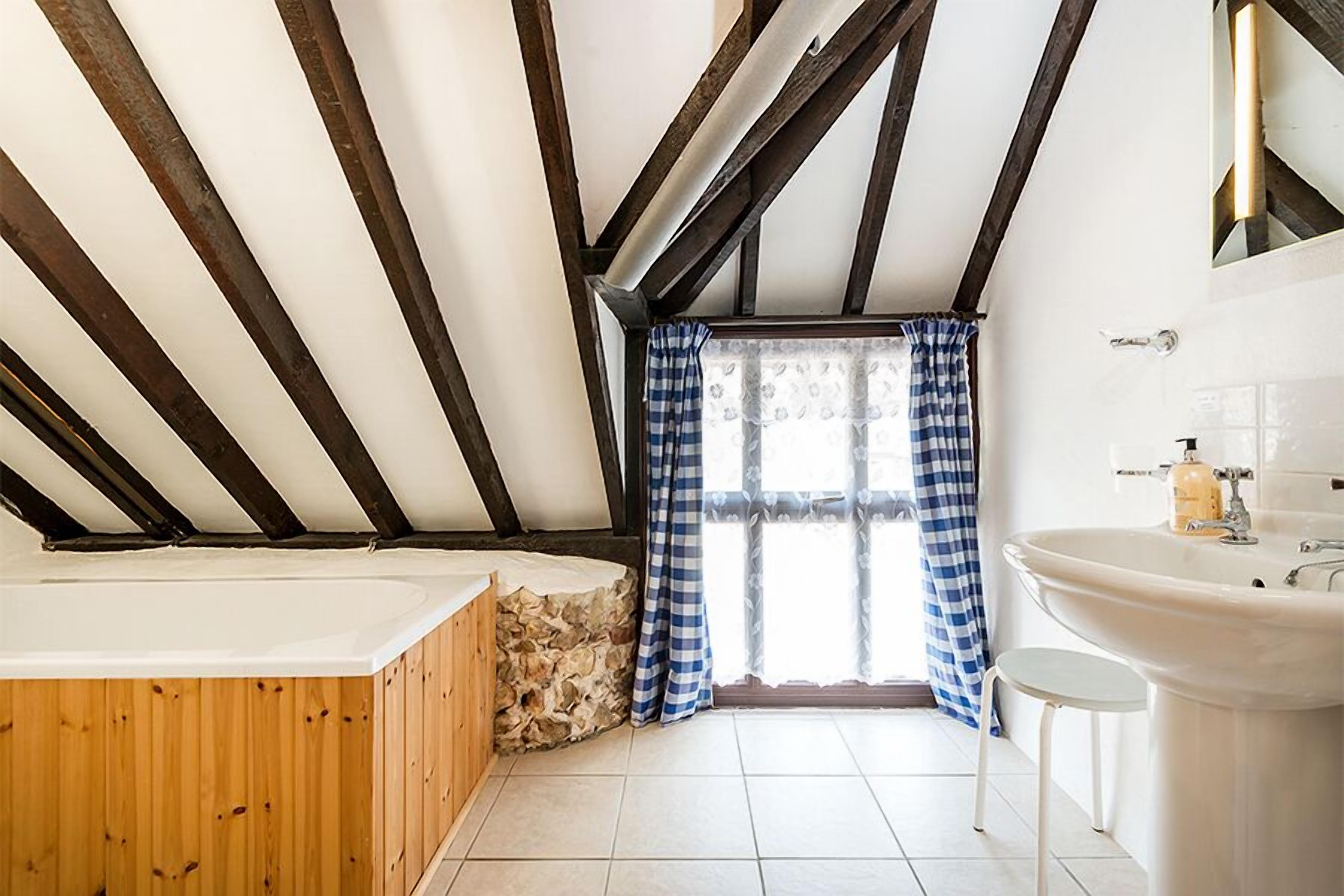 A bathroom with a stone wall, wooden floor, a bathtub, a sink, and a window with blue curtains.