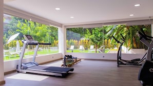Un gimnasio amplio con caminadora, elíptica y bicicleta estática, ventanas grandes con vistas a zonas verdes.
