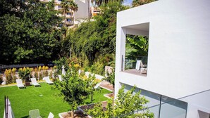 Un edificio moderno con jardín en la azotea, que incluye sillones de sol, una mesa pequeña y plantas en macetas.