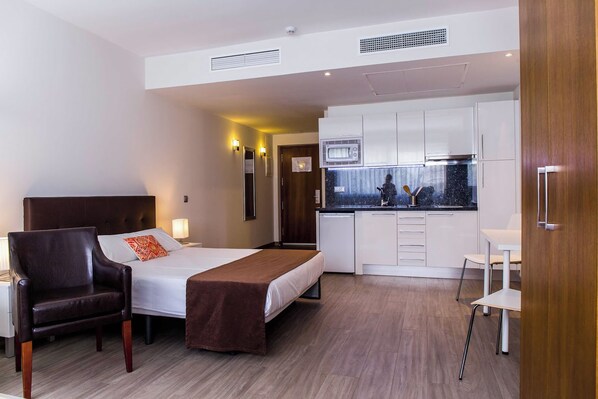 A modern hotel room with a bed, a chair, a desk, and a kitchenette. - BLUESEA Dimona Suites (Torremolinos)