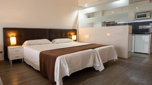 A hotel room with a bed, bedside tables, a nightstand, a kitchenette, and a microwave. - BLUESEA Dimona Suites (Torremolinos)
