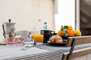 Une table préparée pour le petit-déjeuner, avec une machine à café, des tasses, des verres et une assiette de fruits et de croissants.