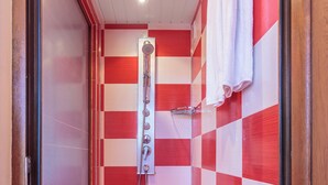 Un baño pequeño con detalles rojos y blancos a cuadros, que incluye una ducha, un perchero y una puerta.