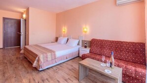 Habitación de hotel con una cama, un sofá rojo, una mesa de centro de madera y dos lámparas de pared.