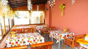 Un restaurante con mesas y sillas de madera, cubiertas con manteles florales.