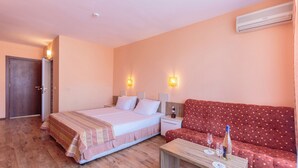 Una habitación de hotel con una cama, un sofá rojo, una mesa de centro de madera y dos lámparas de pared.