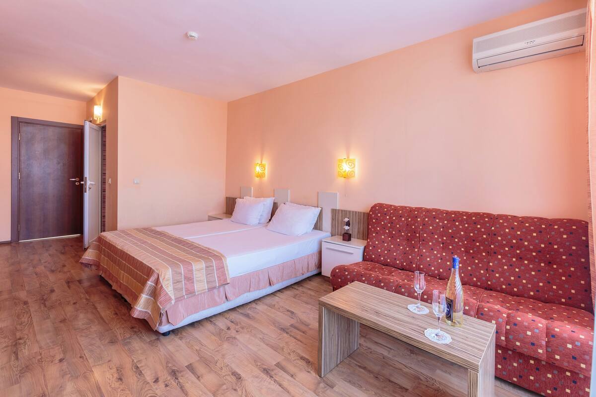 A hotel room with a bed, a red sofa, a wooden coffee table, and two wall-mounted lamps.