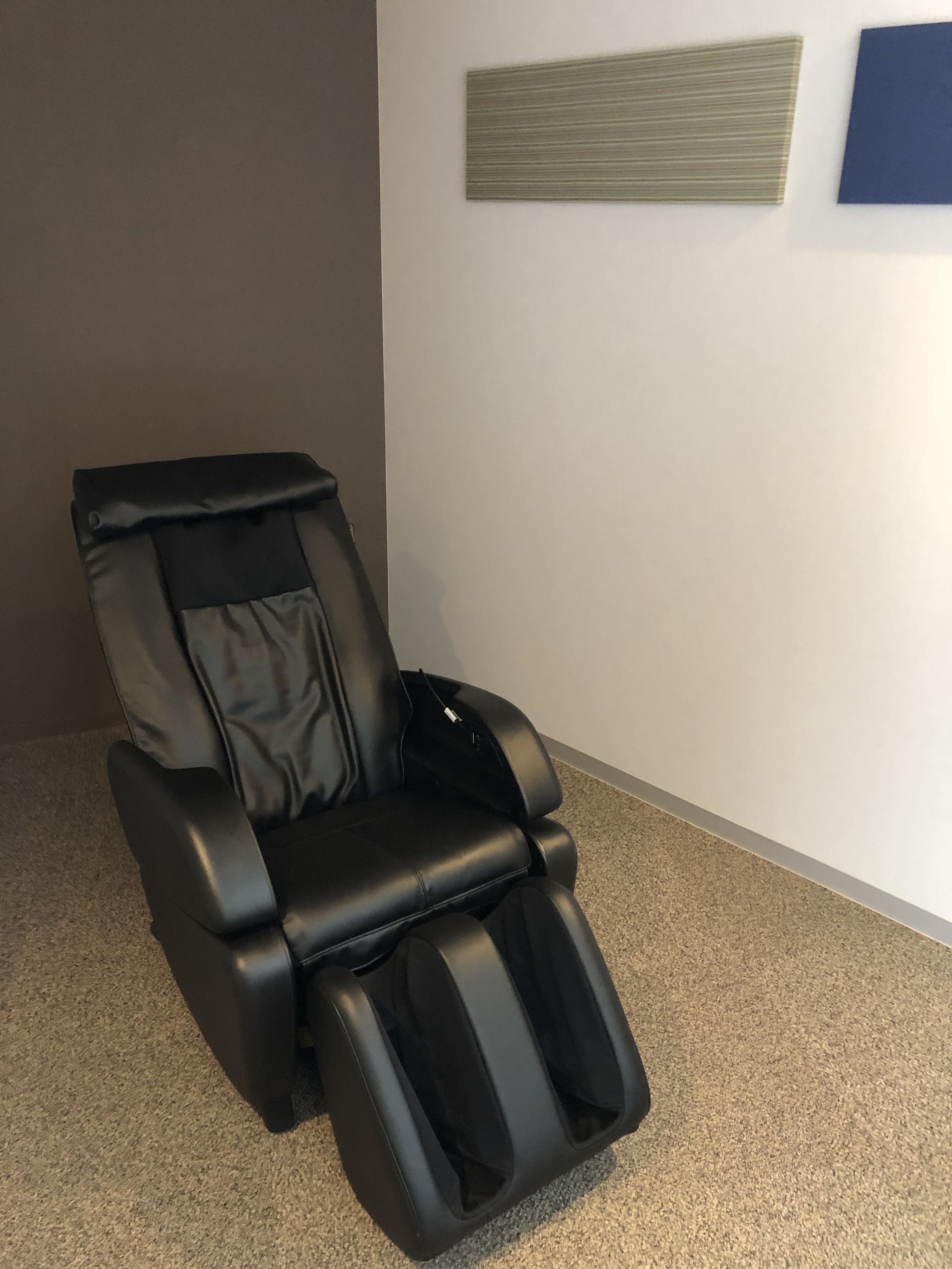 A massage chair in a room with a carpeted floor and a plain wall.