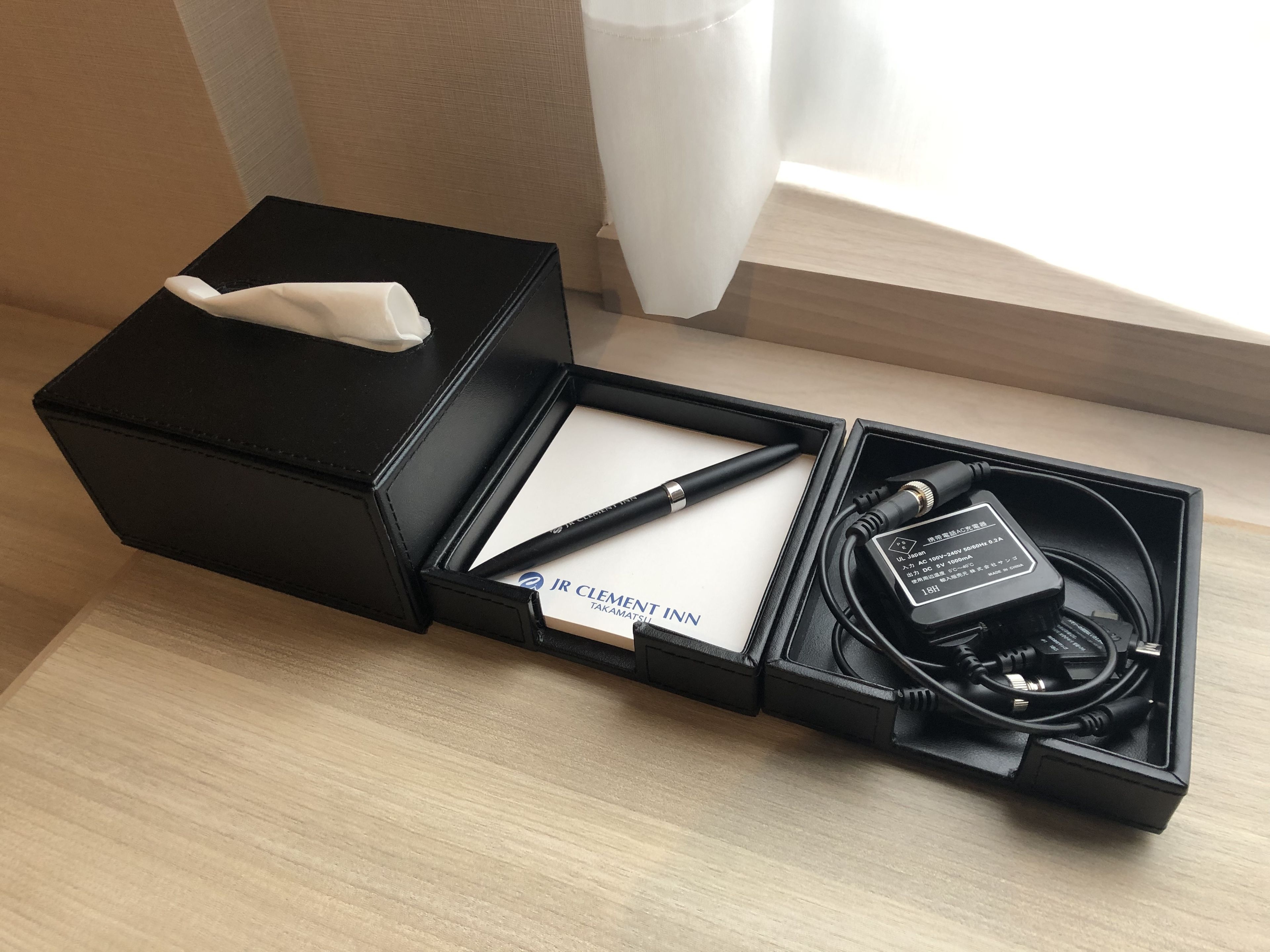 Una caja negra contiene un pañuelo, un bolígrafo, un cuaderno y un adaptador de corriente.