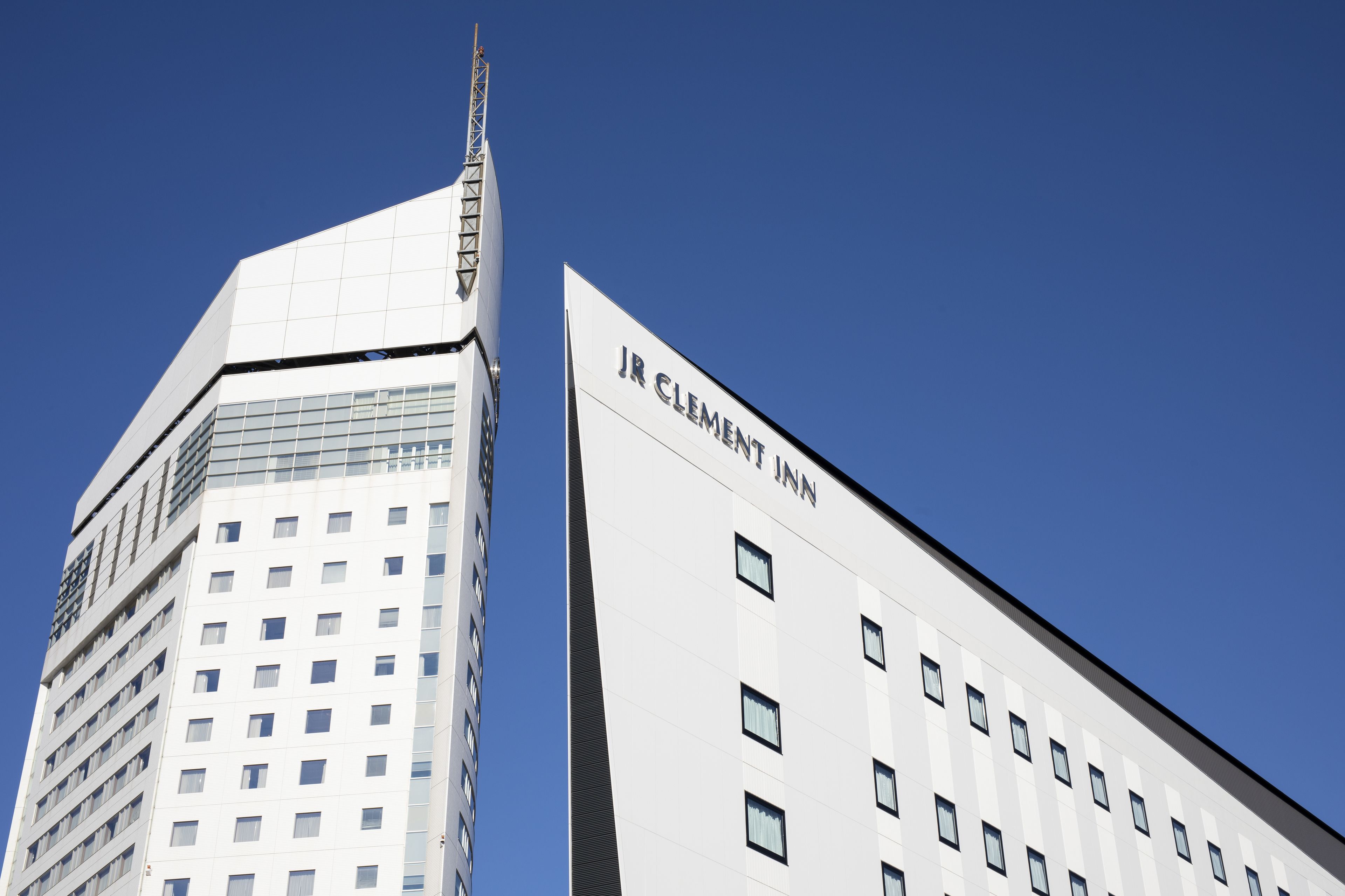 Un bâtiment moderne, facilement reconnaissable grâce à une grande enseigne « JR CLEMENT INN », caractérisé par une façade à motifs géom étriques et un design épuré et anguleux.