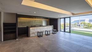 A modern reception area with a marble counter, three stools, and a view of a green field and distant buildings through large windows. - JR Clement Inn Takamatsu (Takamatsu)