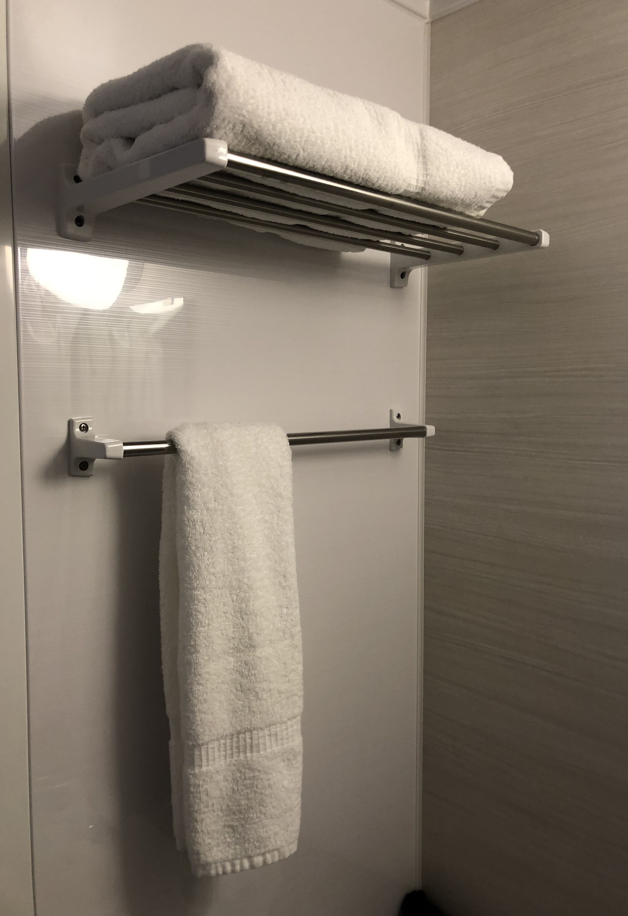 A bathroom with a towel rack holding two folded towels and a towel bar with a single towel.