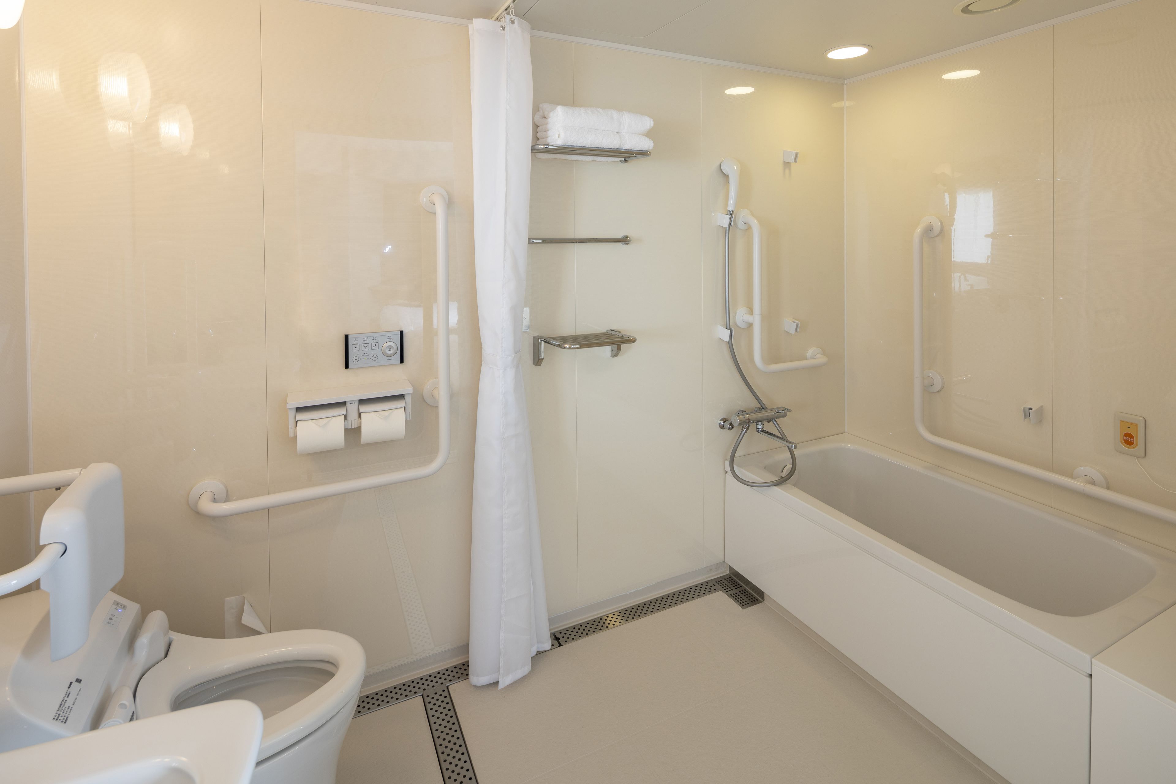 A modern bathroom with a toilet, shower, and bathtub. It includes grab bars, a hand dryer, and a towel rack.