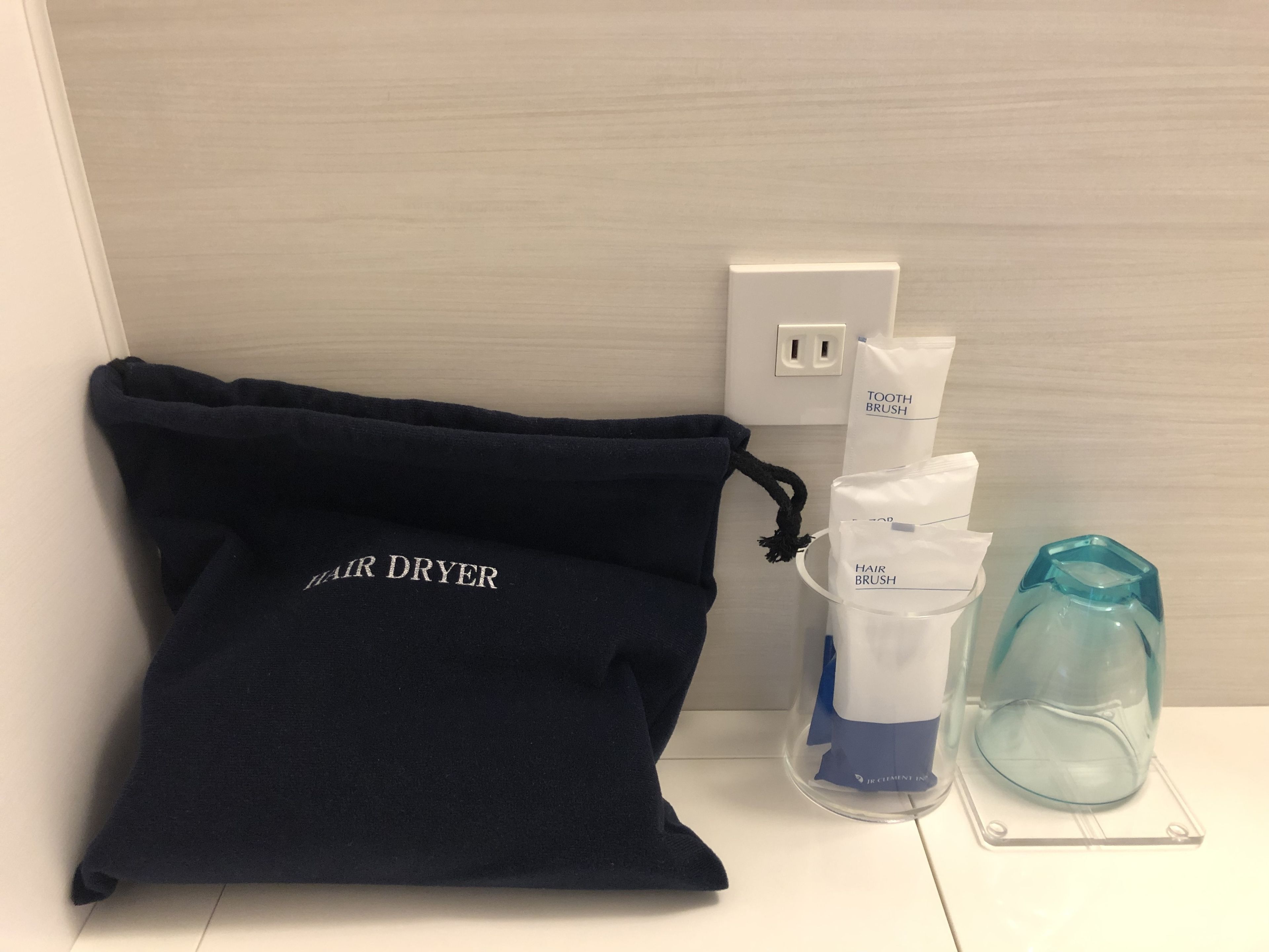 Eine dunkelblaue Haartrockner Tasche, eine Haarbürste und ein Glasbehälter auf weißer Oberfläche.