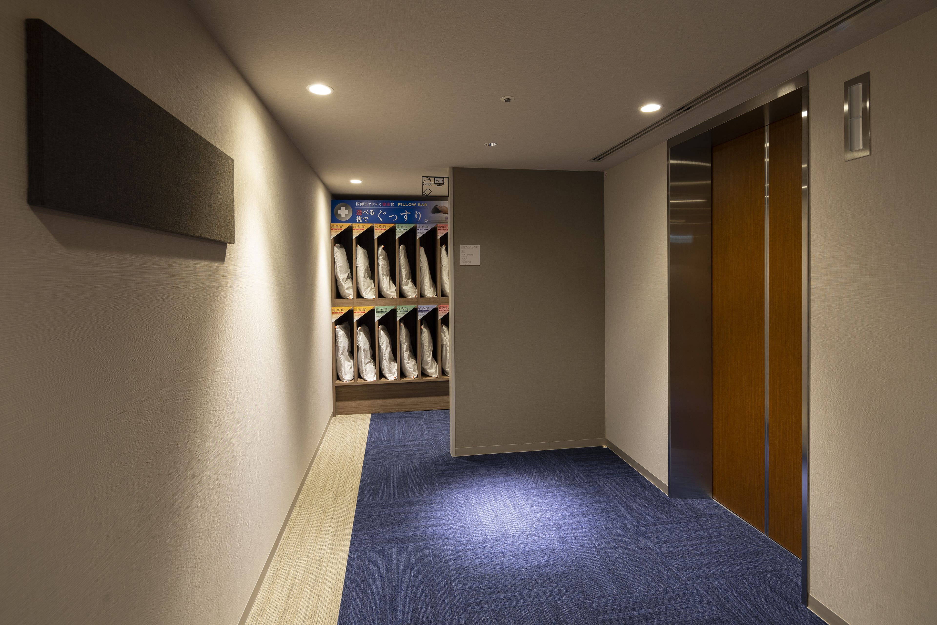 Un couloir avec un tapis bleu, une porte en bois et une étagère fixée au mur où sont posés des sacs.